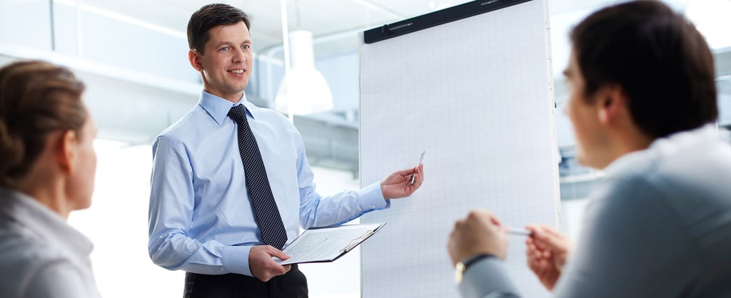 Two people listening to trainer by a flipchart.