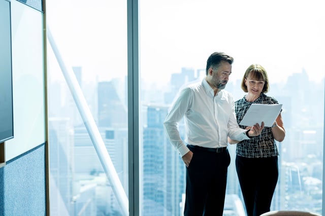 A man and a woman reviewing an environmental audit report, standing near the office window